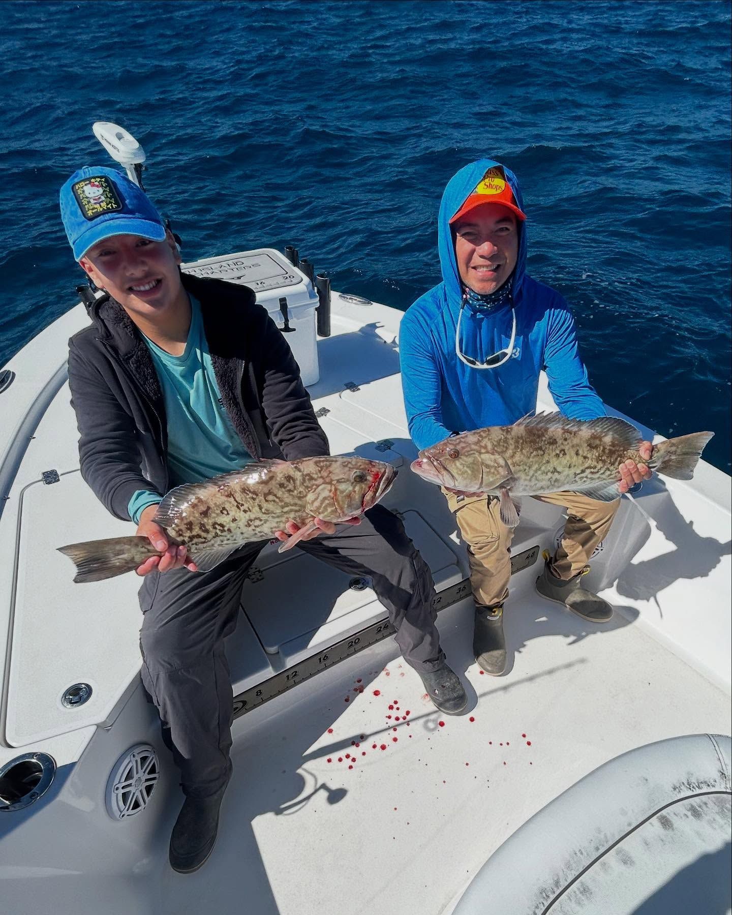 Two men are sitting on a boat holding fish in their hands.