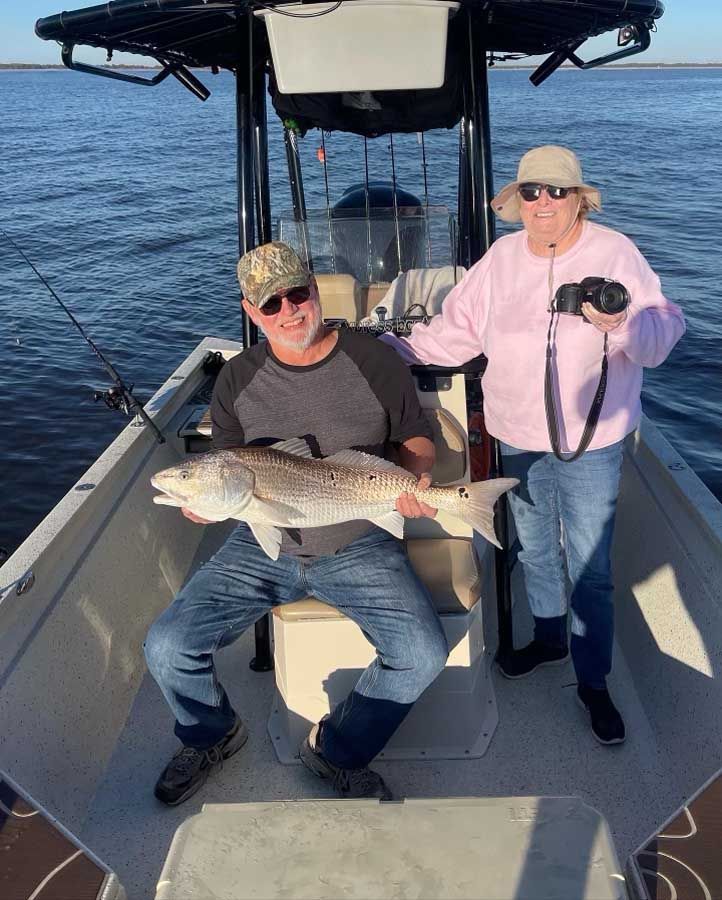 A man and a woman are sitting on a boat holding a large fish.