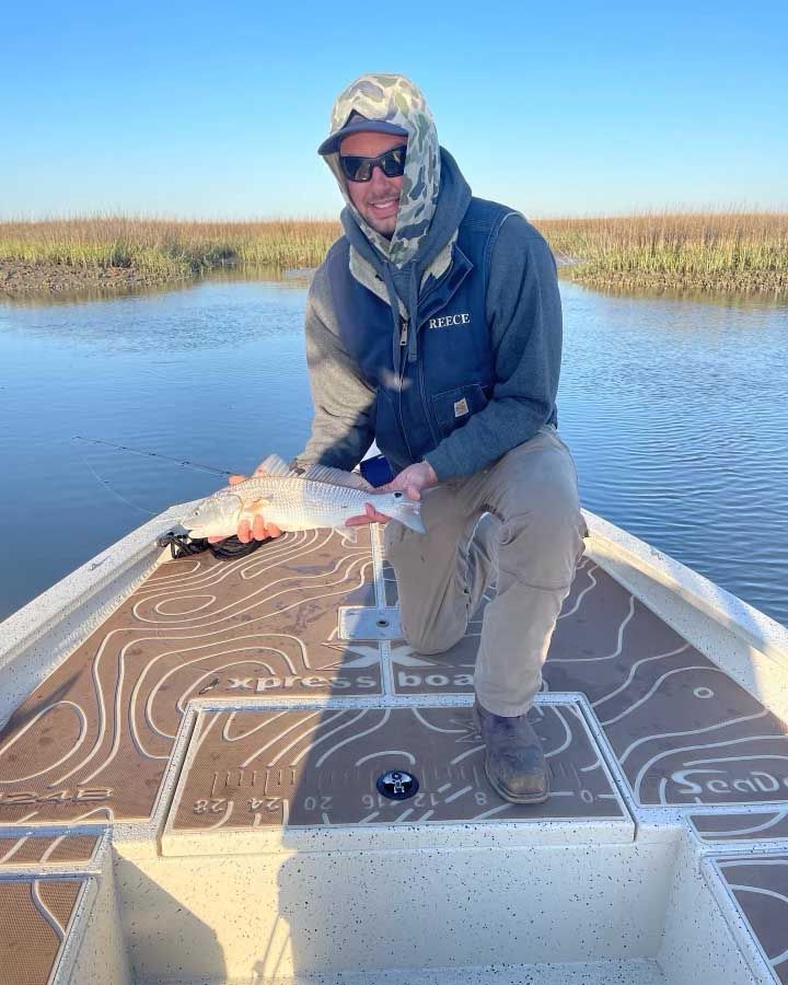 A man is kneeling on the back of a boat holding a fish.