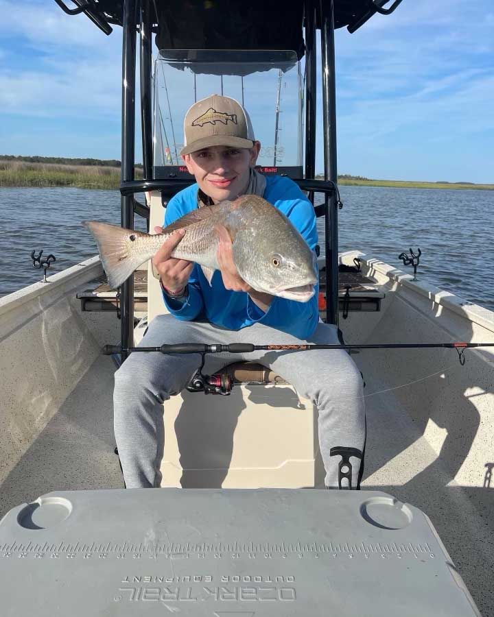 A young man is sitting on a boat holding a large fish.