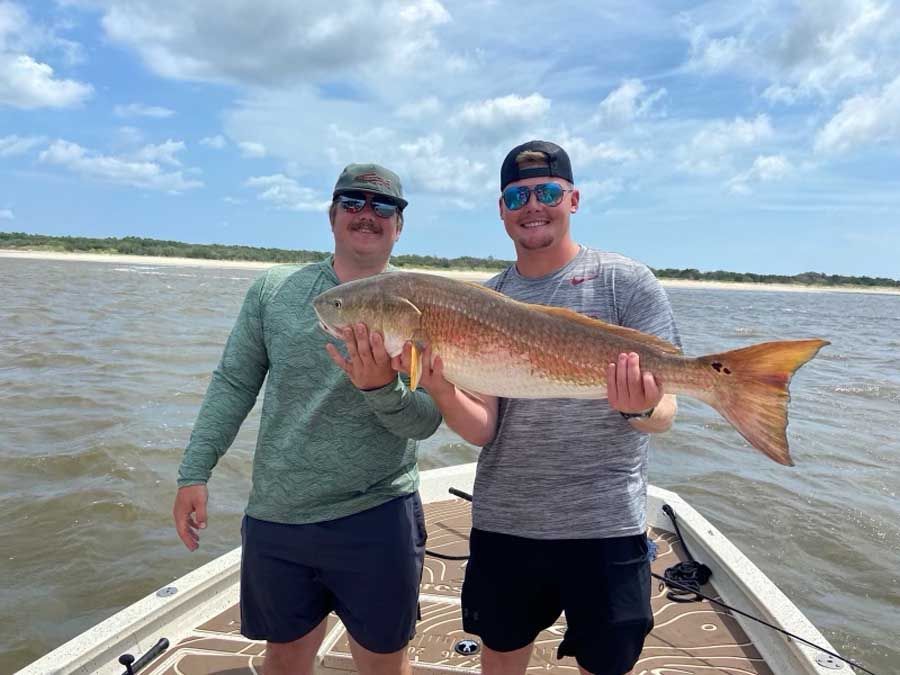 Two men are standing on a boat holding a large fish.