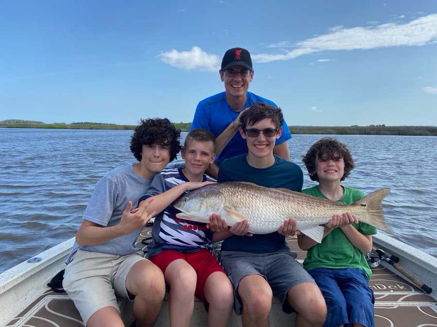 A group of young boys are sitting on a boat holding a large fish.