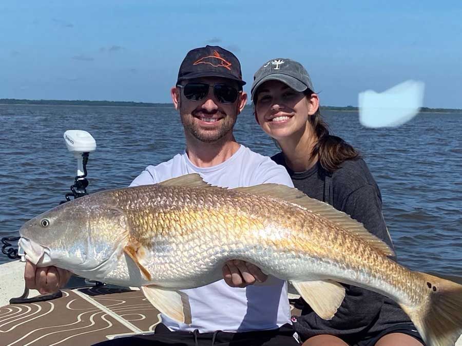 A man and a woman are sitting on a boat holding a large fish.