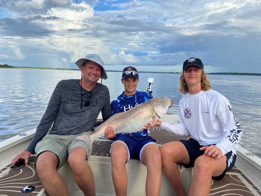 Three men are sitting on a boat holding a large fish.