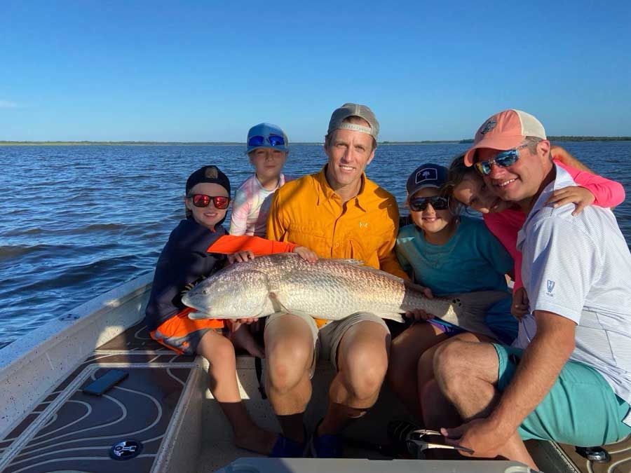 A group of people are sitting on a boat holding a large fish.