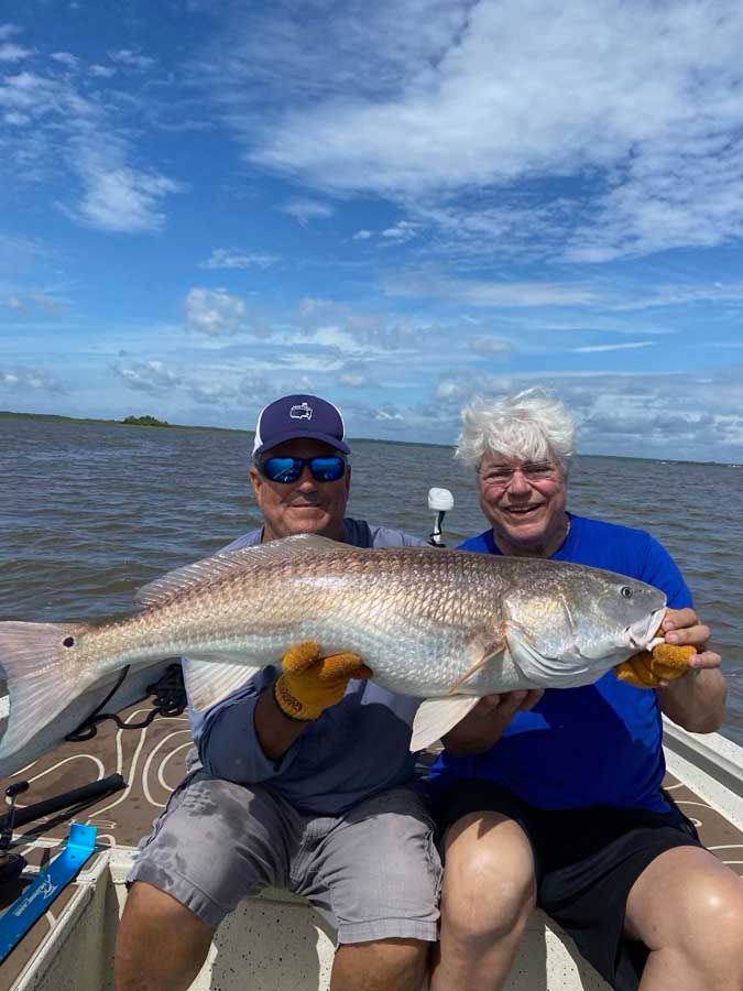 Two men are sitting on a boat holding a large fish.