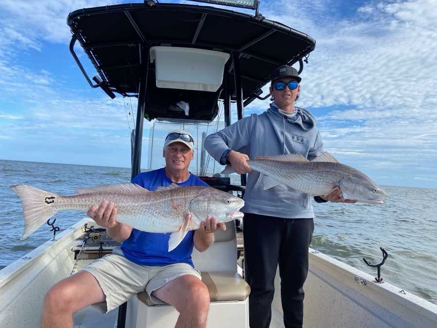Two men are sitting on a boat holding two large fish.
