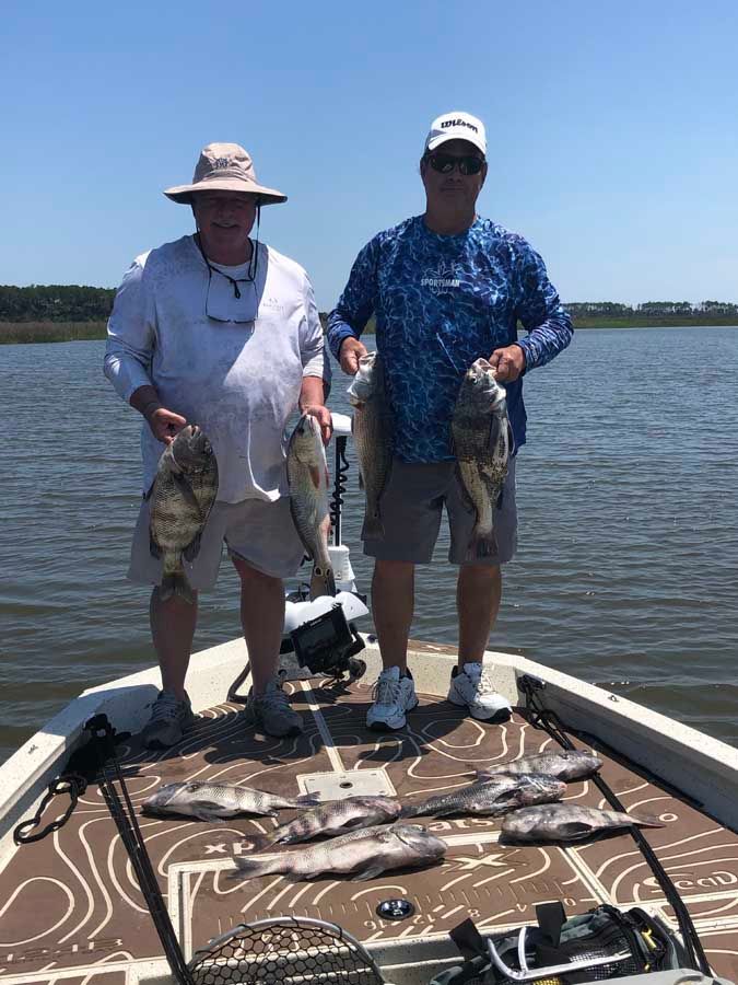 Two men are standing on a boat holding fish.