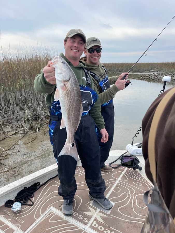 Two men are standing on a boat holding a fish.