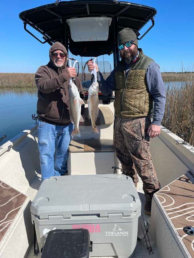 Two men are standing on a boat holding fish.