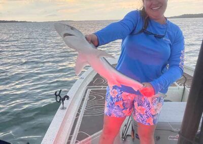 A woman is standing on a boat holding a shark.
