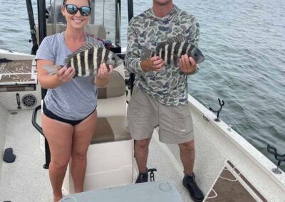A man and a woman are holding fish on a boat.