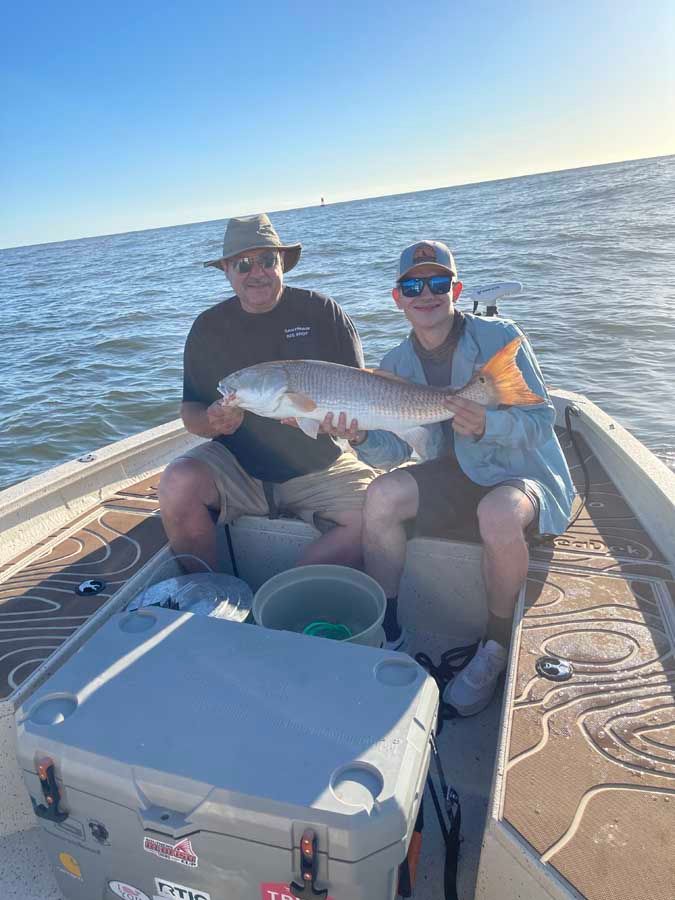 Two men are sitting on a boat holding a large fish.
