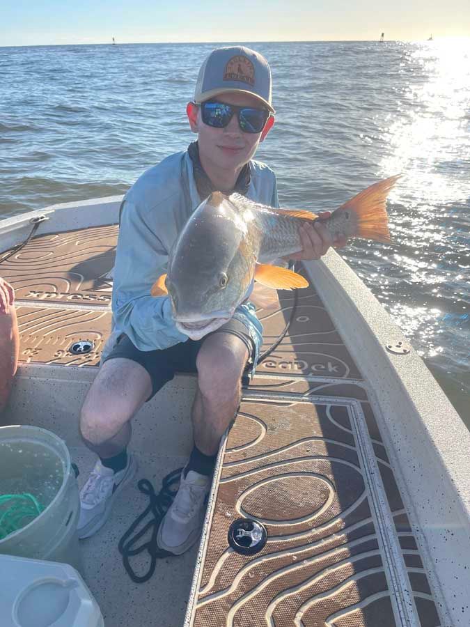 A young boy is sitting on a boat holding a large fish.