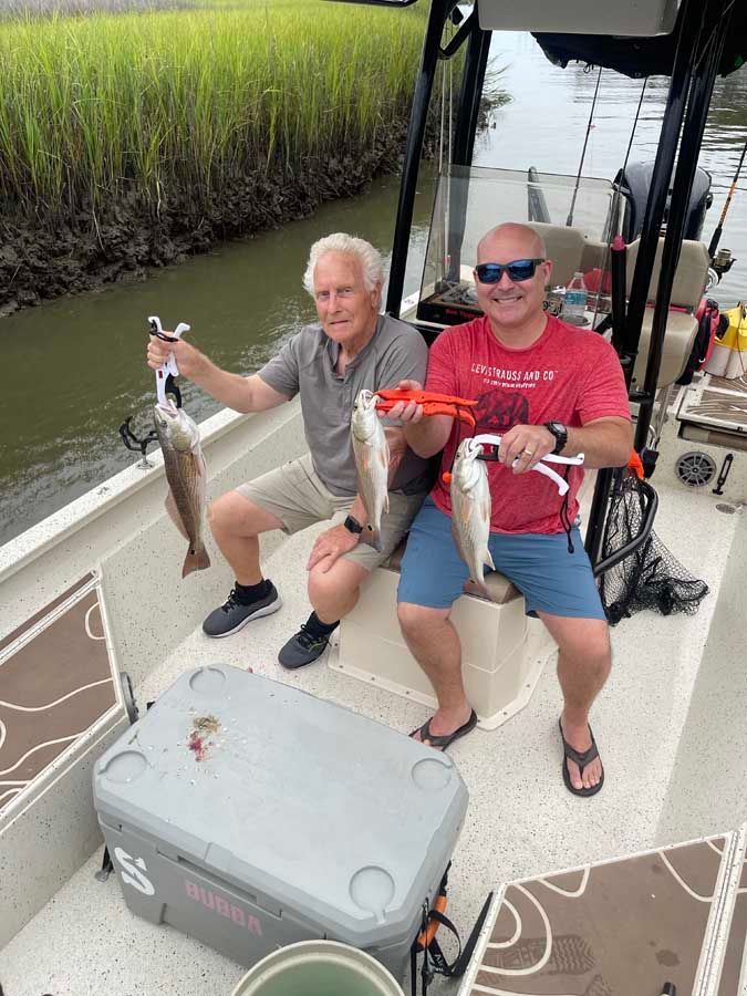 Two men are sitting on a boat holding fish.