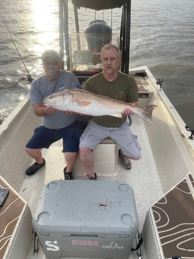 Two men are sitting on a boat holding a large fish.