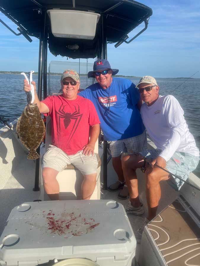 Three men are sitting on a boat holding a fish.