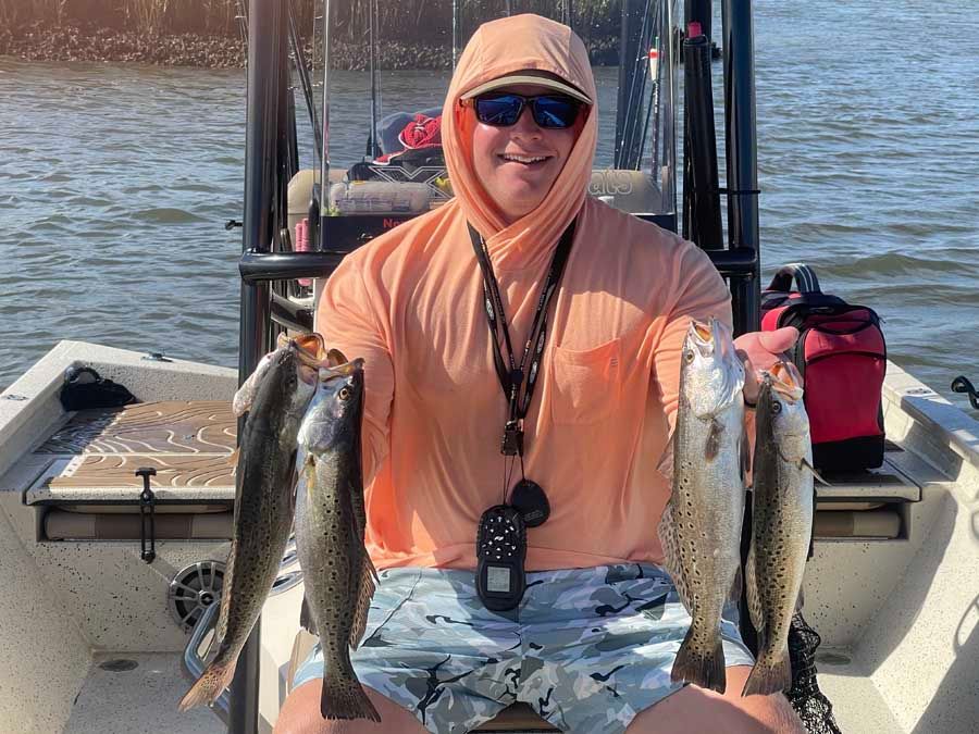 A man is sitting on a boat holding three fish.