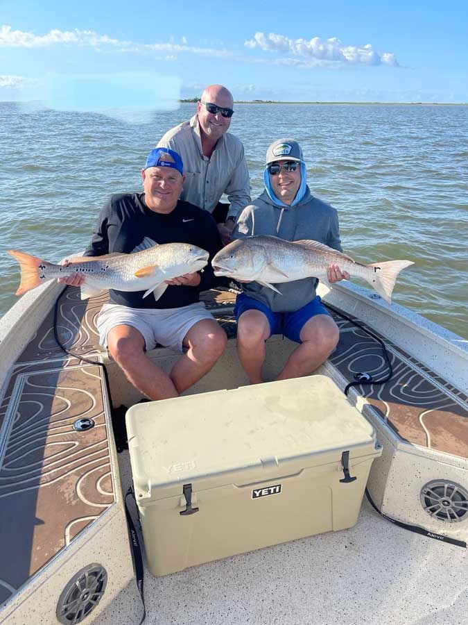 Three men are sitting on a boat holding fish.