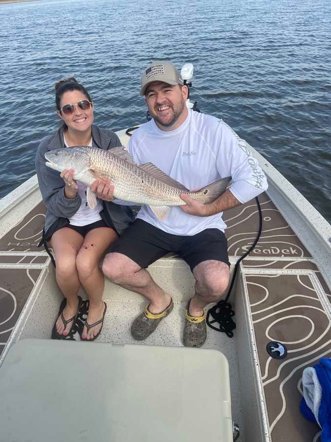 A man and a woman are sitting on a boat holding a large fish.