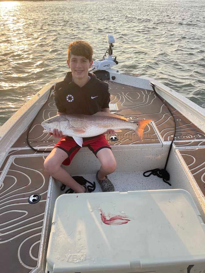 A young boy is sitting in a boat holding a large fish.