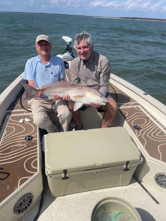 Two men are sitting on a boat holding a large fish.