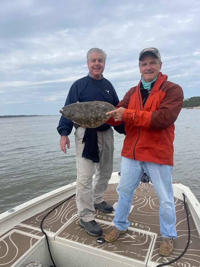 Two men are standing on a boat holding a large fish.