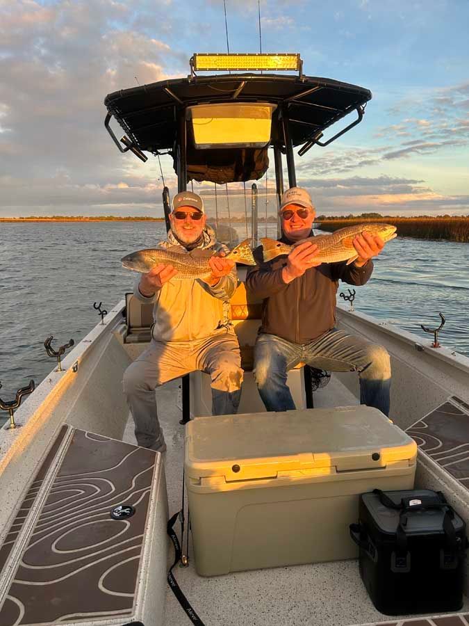 Two men are sitting on a boat holding fish.