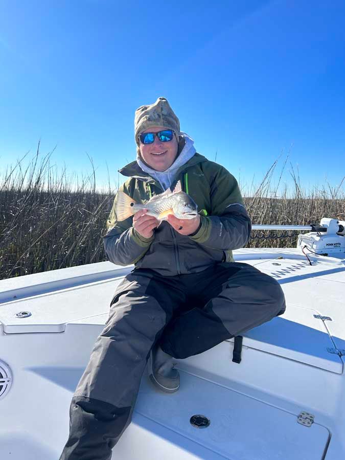 A man is sitting on the back of a boat holding a fish.