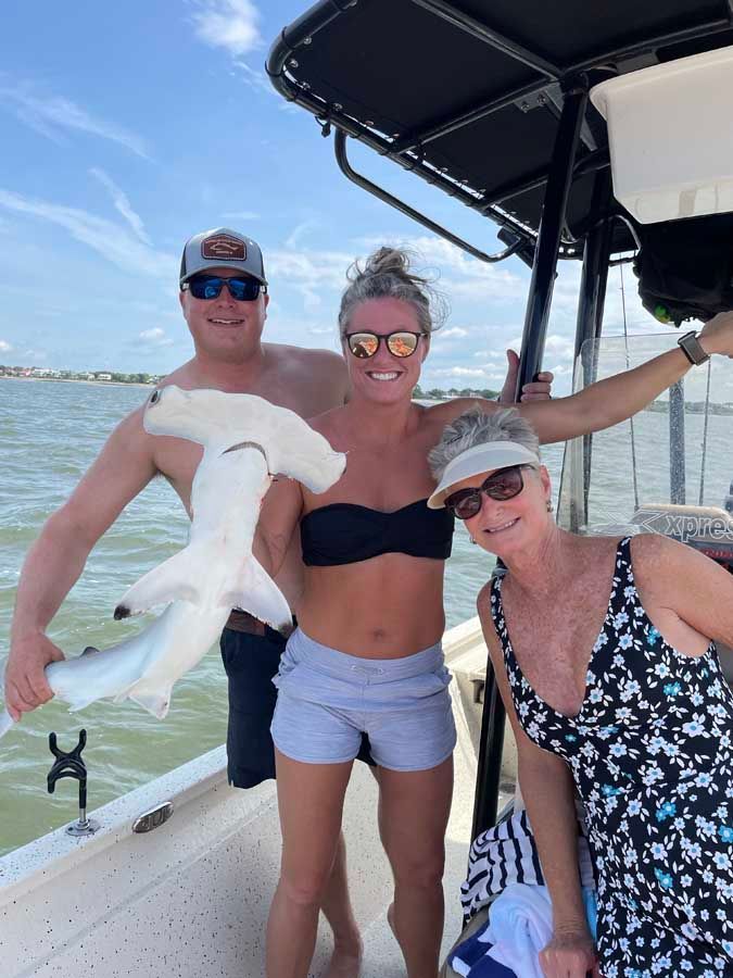 A man and two women are standing on a boat holding a hammerhead shark.