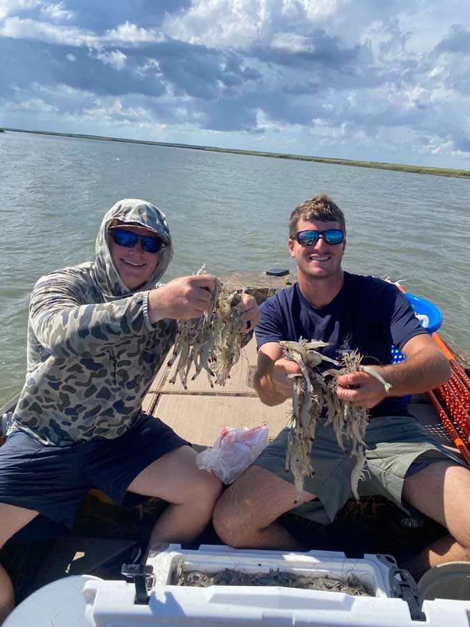 Two men are sitting on a boat holding shrimp.