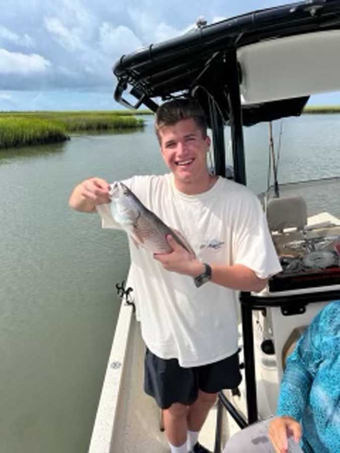 A young man is standing on a boat holding a fish.