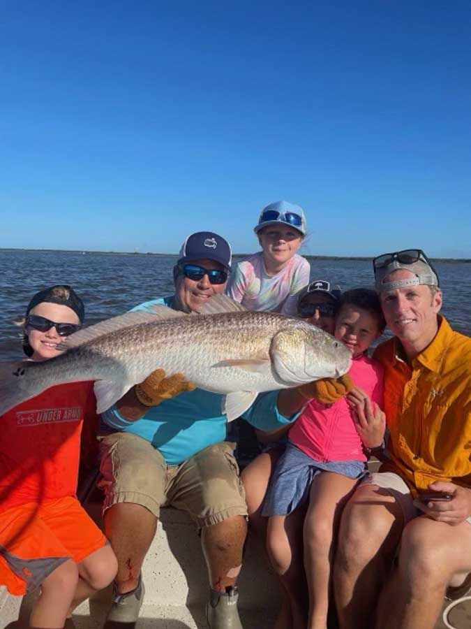 A group of people are sitting on a boat holding a large fish.