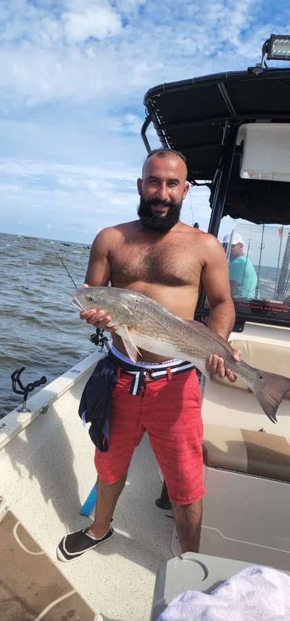 A shirtless man is standing on a boat holding a large fish.