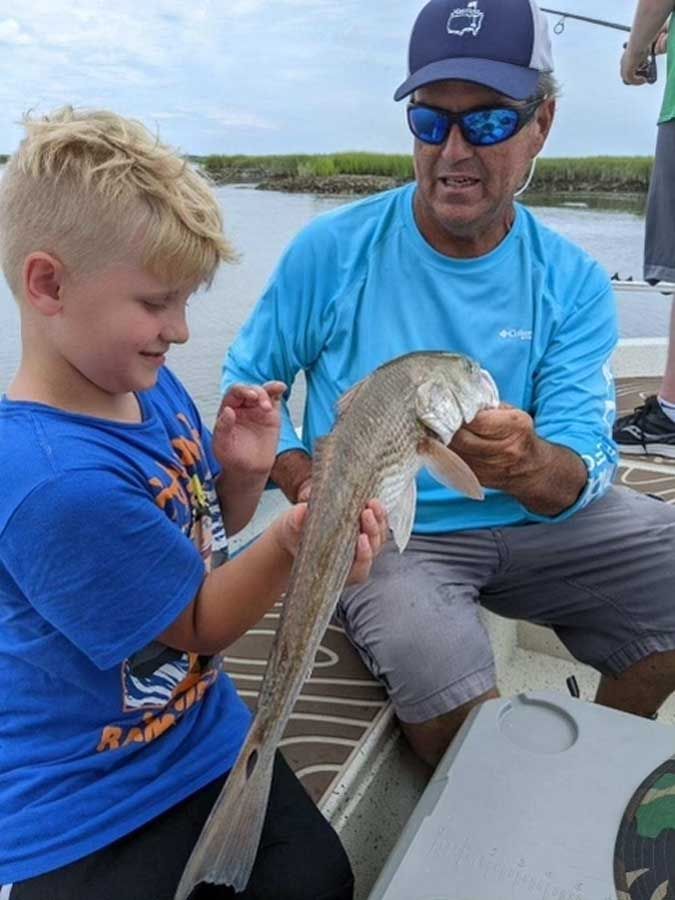 A man and a boy are sitting on a boat holding a fish.