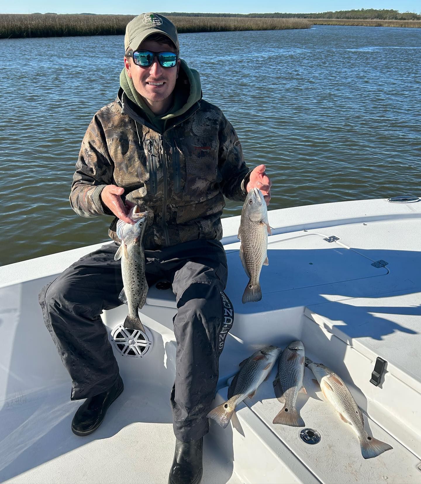 A man is sitting on a boat holding two fish in his hands.