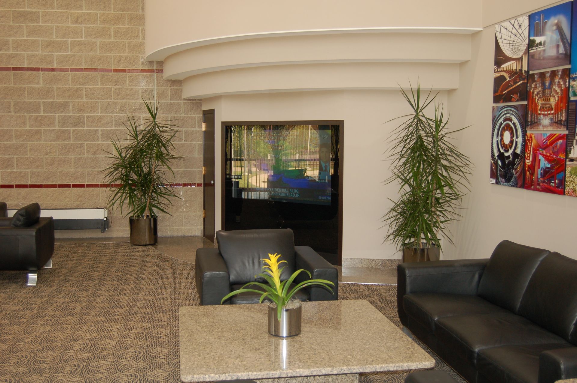 Lobby with seating, plants, and a doorway. Beige brick wall, marble floors, and colorful artwork on the wall.