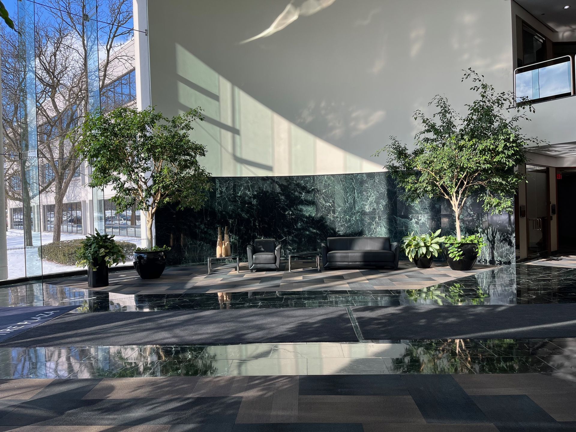 Interior lobby with trees, seating, and a water feature. Sunlight reflects on the polished floor.