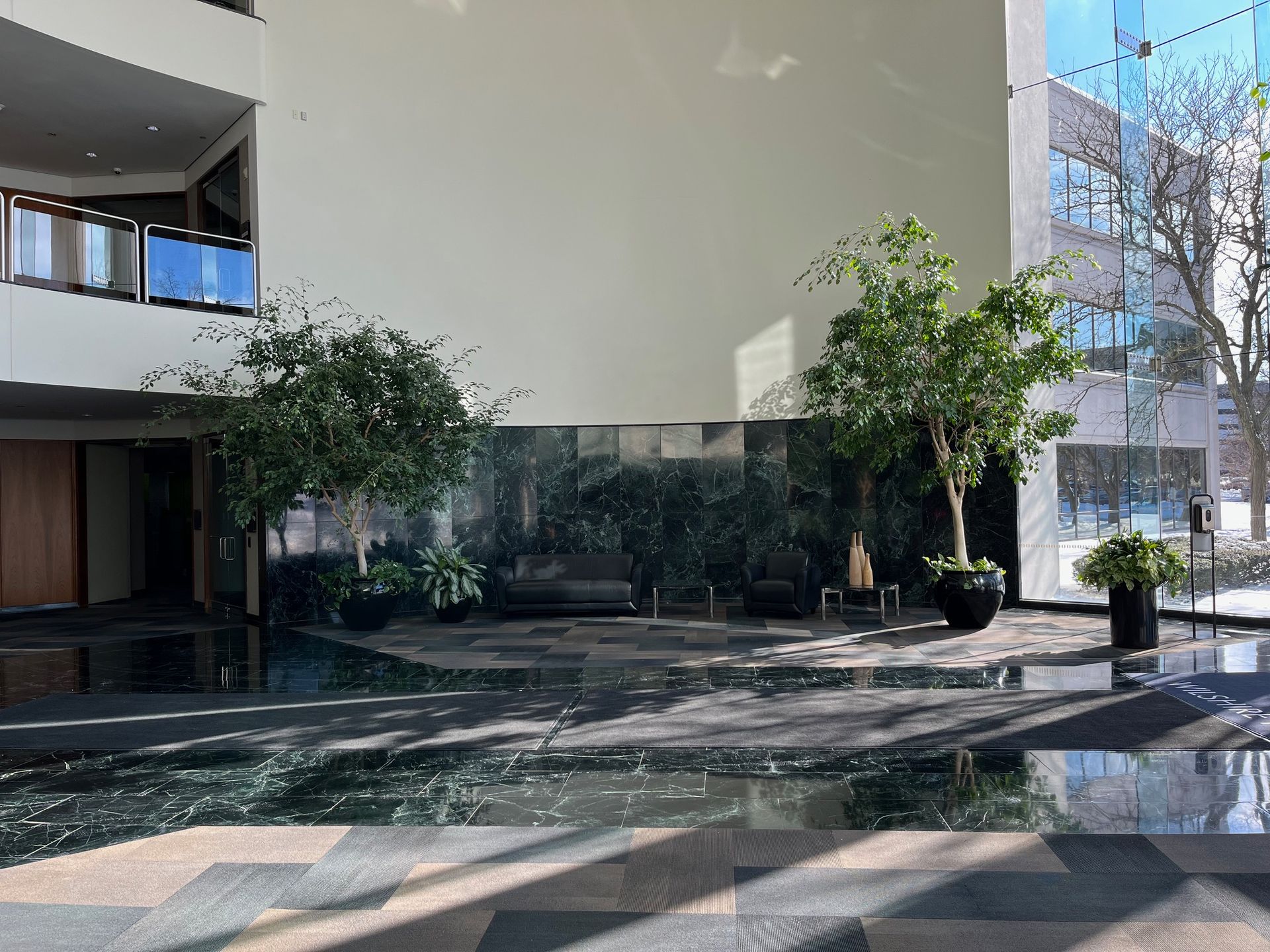 Indoor lobby with trees and marble flooring, natural light through windows.