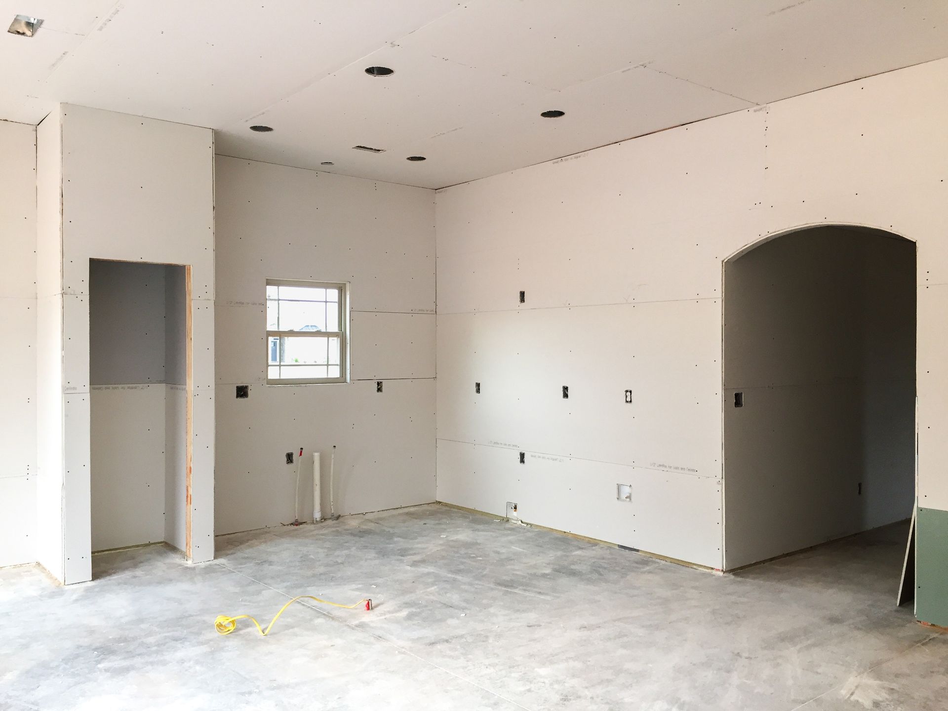 Two workers installing drywall on a ceiling in a room under construction; stacks of drywall on the floor.