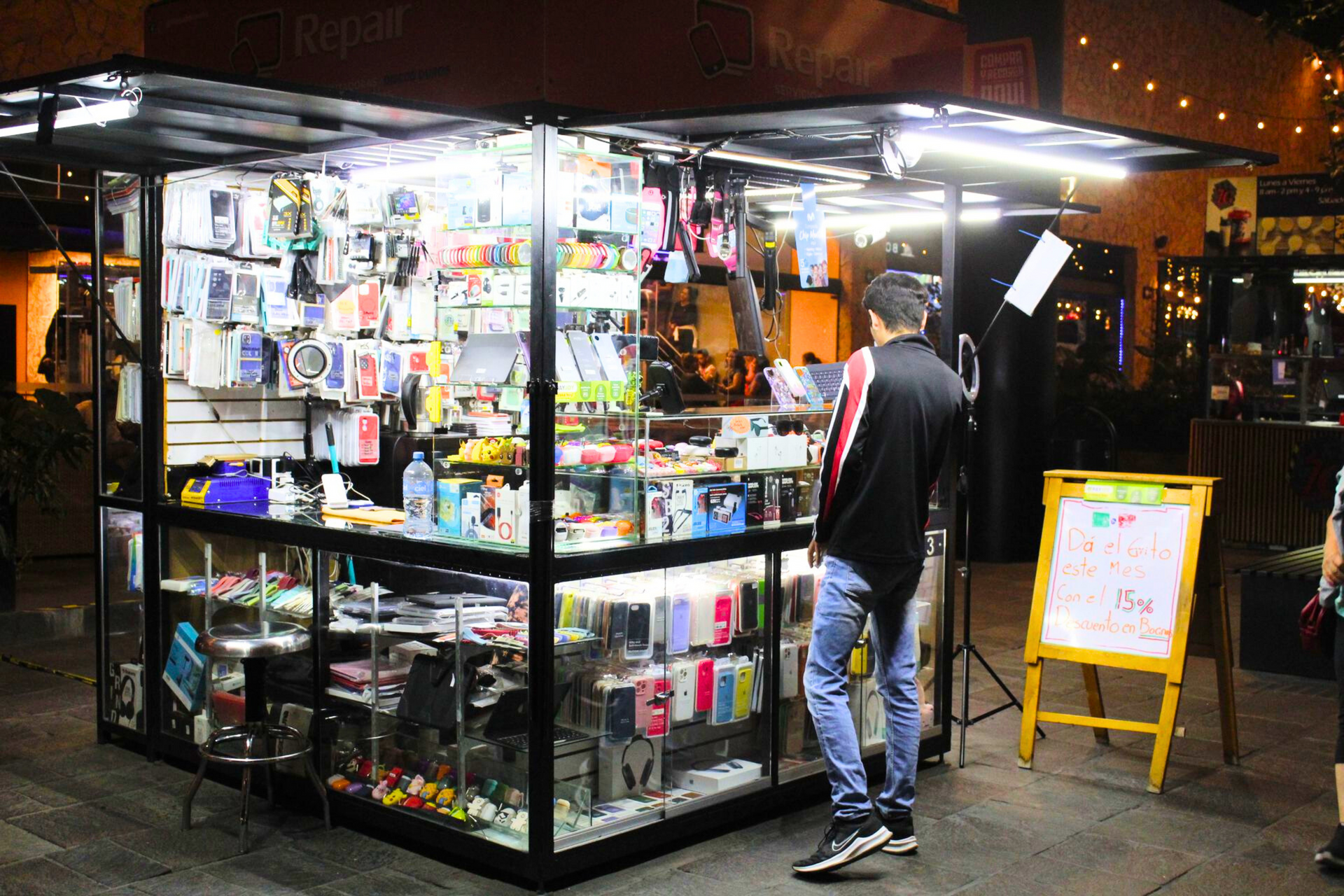 Un hombre está parado frente a un quiosco que vende accesorios para teléfonos celulares.