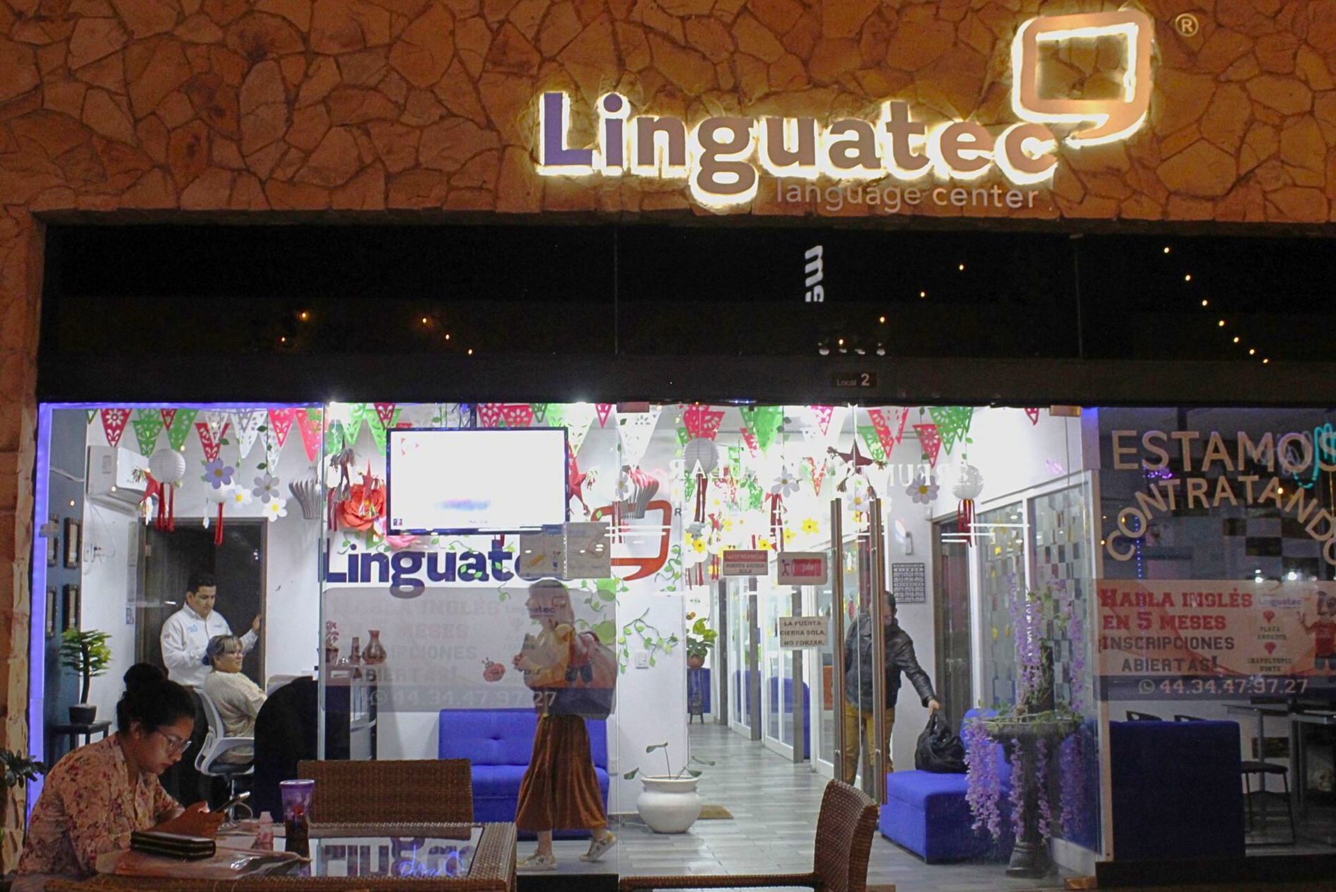 Una mujer está sentada en una mesa frente a una tienda llamada linguatec