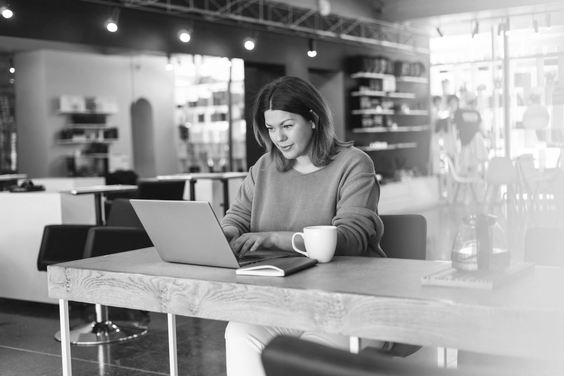 Woman at a salon reception desk with laptop and paperwork, surrounded by beauty products.