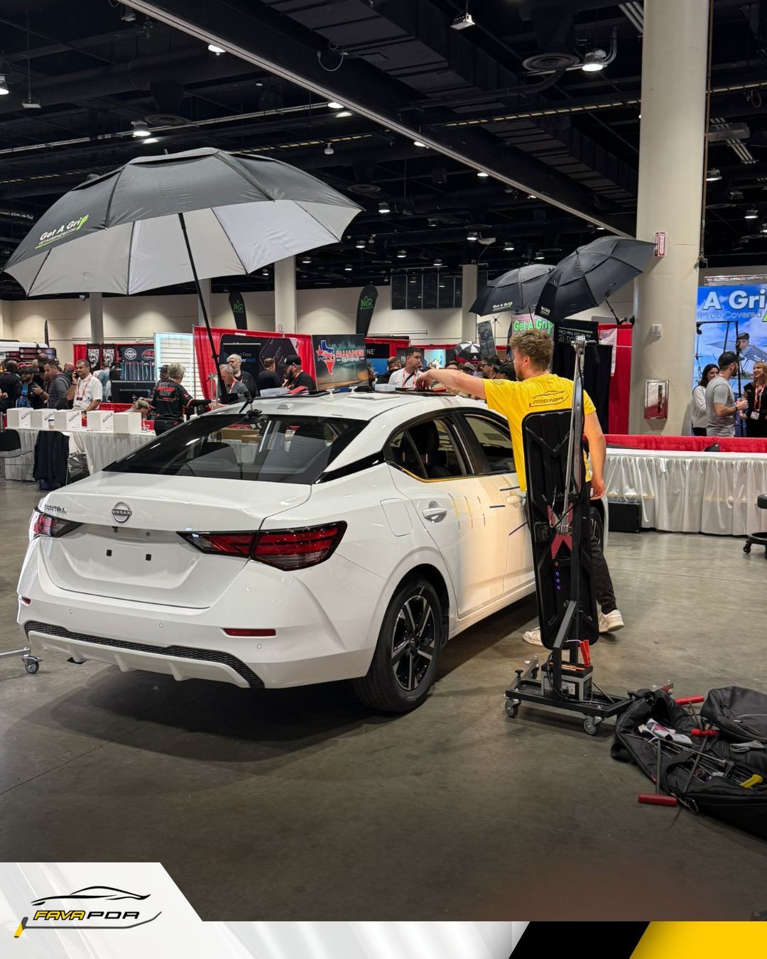 White car at an expo, being filmed with lights. Person adjusts equipment.