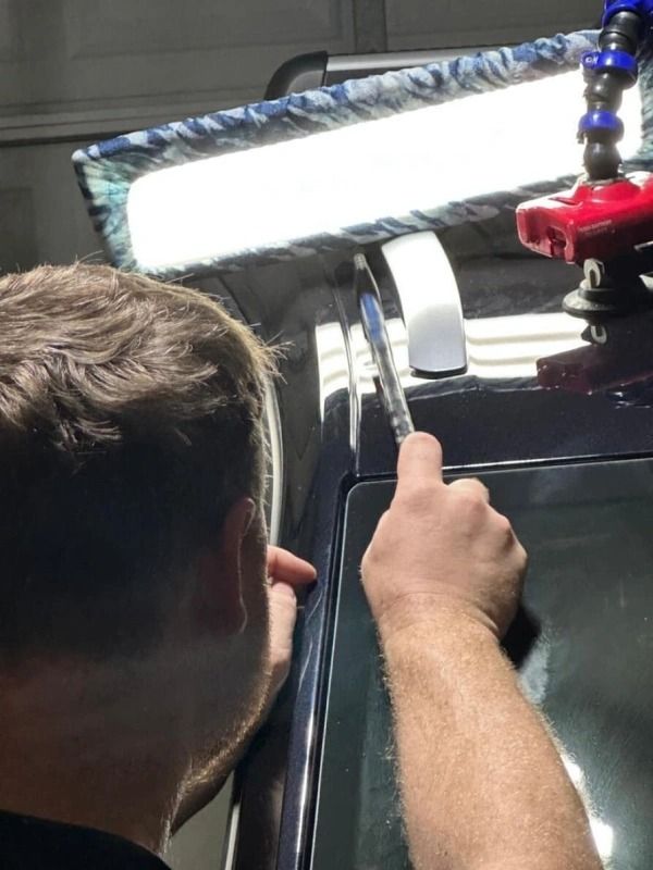 Person using a pen to inspect car dent under a bright inspection light in a garage.