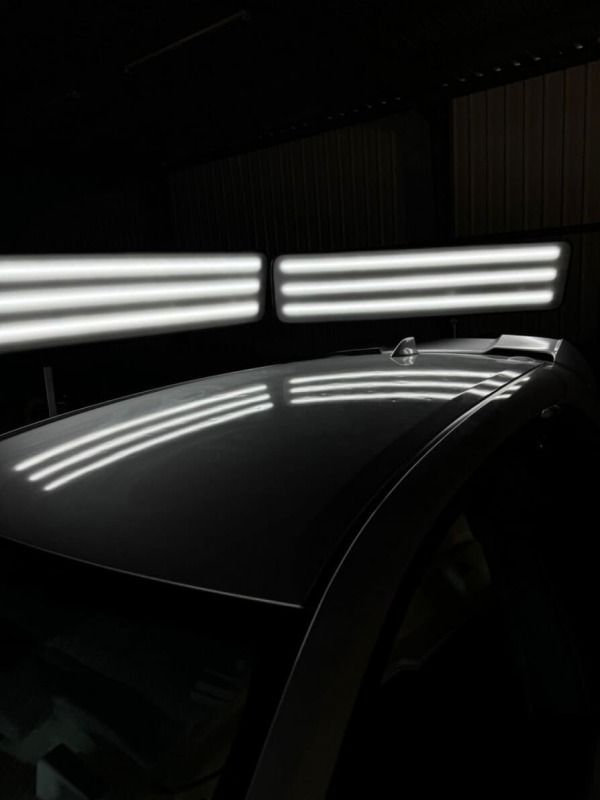 Car roof under bright lights, showing reflections used to detect dents.