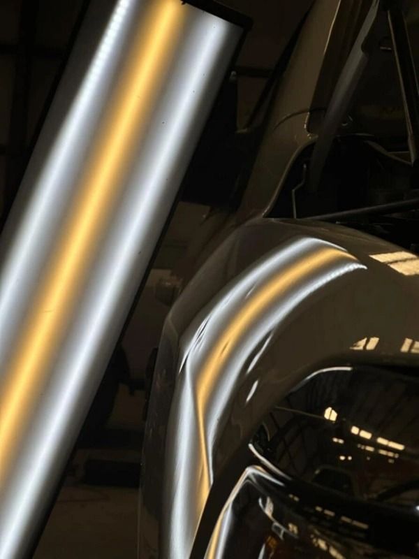 White car panel with dent, lit by a reflection board for paintless dent removal.