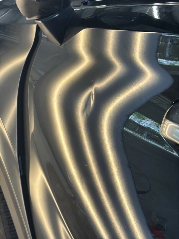 Car door with a dent, light reflecting off the damaged surface creating wavy patterns.