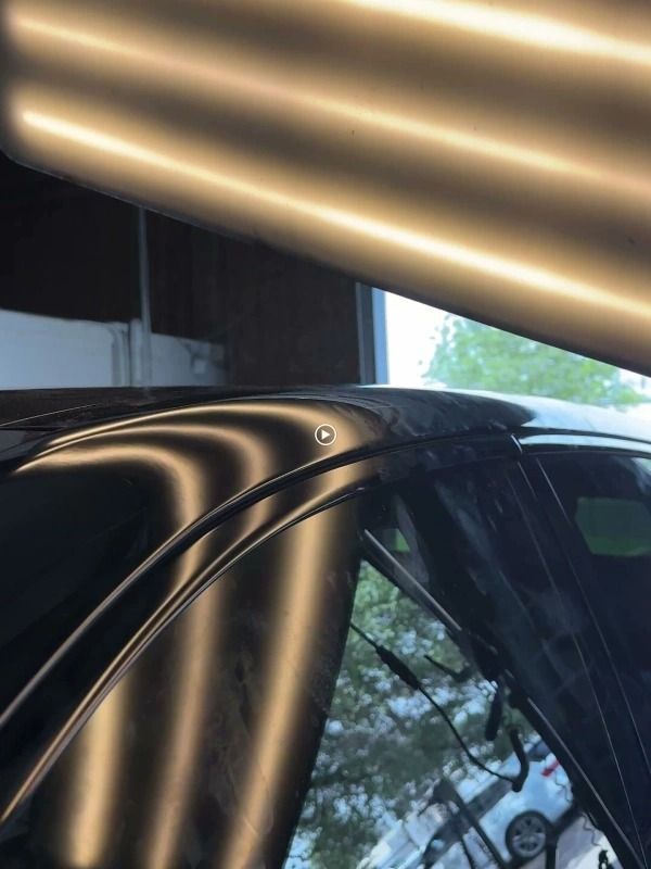 Black car roof with a dent illuminated by a fluorescent light; dent repair in progress.