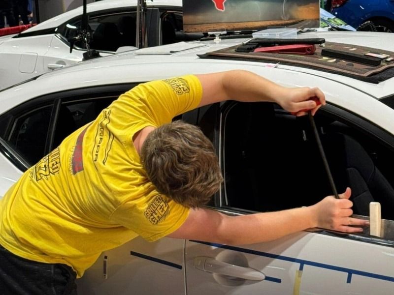 Man in yellow shirt installing window tint on a white car.